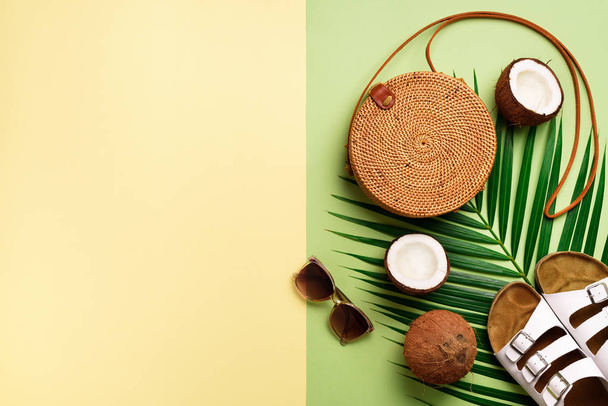 Stylish rattan bag, coconut, birkenstocks, palm branches, sunglasses on olive green background. Banner. Top view with copy space. Trendy bamboo bag and white shoes. Summer fashion flat lay - 写真・画像