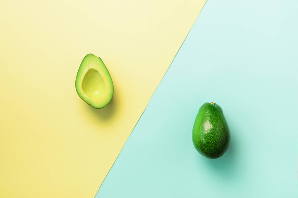 Avocado sliced with seed, whole fruit on blue and yellow background. Top view. Pop art design, creative summer food concept. Minimal flat lay style. - Foto, Imagen
