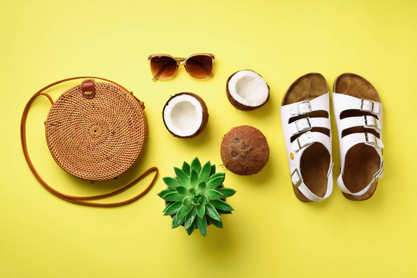 Stylish rattan bag, coconut, birkenstocks, palm branches, succulent, sunglasses on yellow background. Banner. Top view with copy space. Trendy bamboo bag and white shoes. Summer fashion flat lay - Foto, immagini