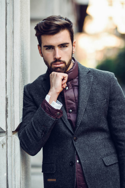 Młody Brodaty mężczyzna, model mody, w wielkomiejskim sobie brytyjski elegancki garnitur. Facet z brodą i nowoczesną fryzurę na ulicy. - Zdjęcie, obraz