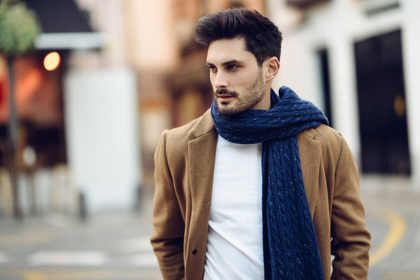 Jeune homme portant des vêtements d'hiver dans la rue. Jeune homme barbu avec coiffure moderne avec manteau, écharpe, jean bleu et t-shirt. - Photo, image