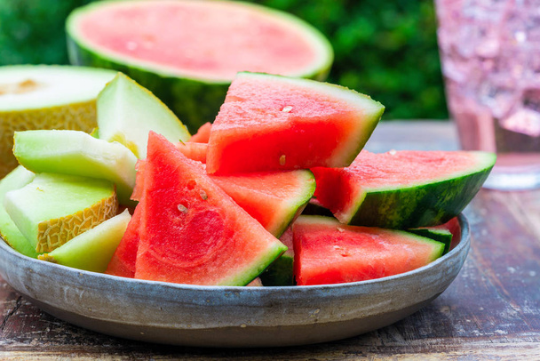 Slices of sweet, refreshing watermelon and honeydew melon on a garden table. Summer outdoor eating. - Foto, immagini