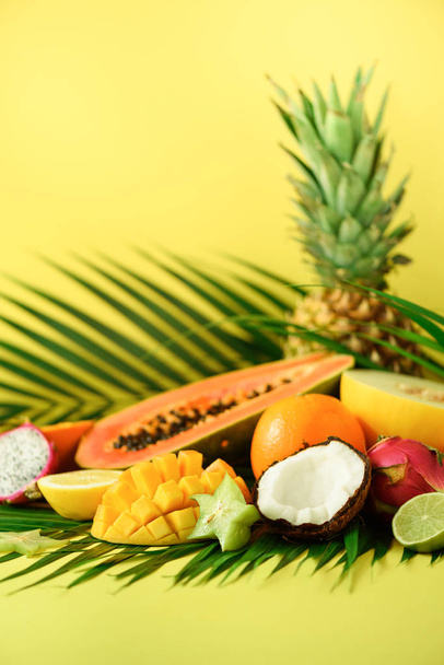 Assortment of exotic fruits on yellow background. Detox, vegan food, summer concept. Papaya, mango, pineapple, carambola, dragon fruit, kiwi, orange, melon, coconut, lime over palm leaves. - Foto, afbeelding