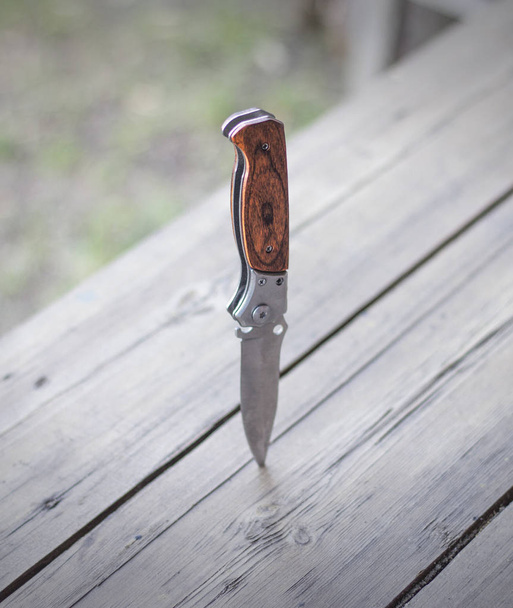 Folding knife stuck in a wooden table, close-up - Фото, изображение
