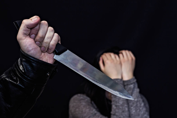 A man's hand with a knife, in the background a girl is crying, a black background - Foto, Imagen