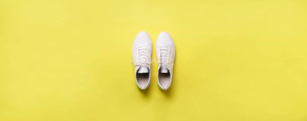 Stylish white sneakers and rope on yellow background with copy space. Top view. Minimal flat lay. Summer shoes collection. First step concept. Banner - Fotó, kép
