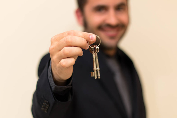 Mies kiinteistönvälittäjä hymyilee luovuttaessaan avaimia onnistuneen myynnin jälkeen
 - Valokuva, kuva