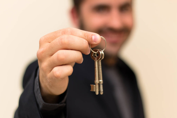 Erkek başarılı bir satış sonrası anahtarlarını teslim ederken gülümseyen emlakçı - Fotoğraf, Görsel