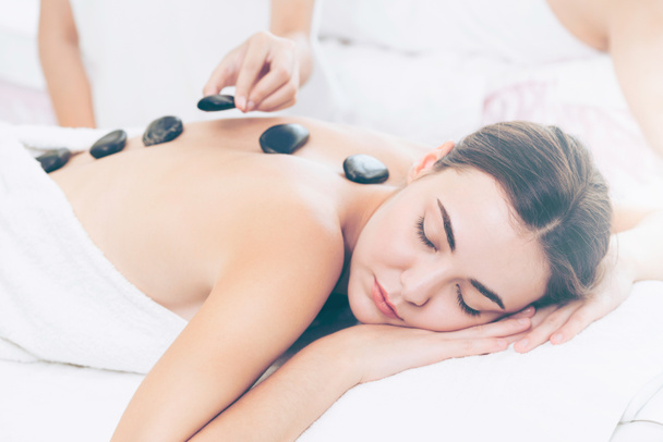 Woman getting hot stone massage treatment by professional beautician therapist in spa salon. Luxury wellness, back stress relief and rejuvenation concept. - Foto, Imagen