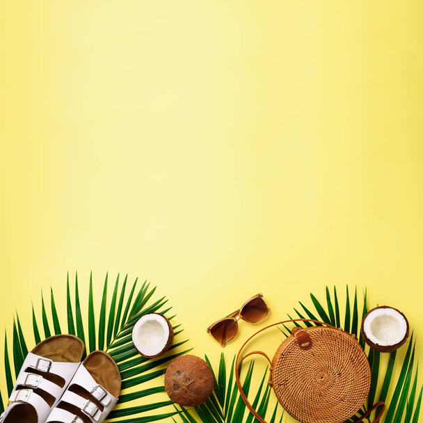 Round rattan bag, coconut, birkenstocks, palm branches, sunglasses on yellow background. Square crop. Top view, copy space. Trendy bamboo bag and shoes. Summer fashion flat lay. Trip, vacation concept - Zdjęcie, obraz