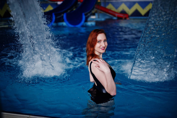 Sexy red haired girl in black swimsuit having rest in swimming pool of aqua park. - Photo, Image