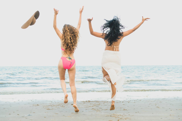 Szczęśliwe kobiety w bikini skoki w powietrzu razem na tropikalnej plaży piasek w letnie wakacje. Podróż życia. - Zdjęcie, obraz