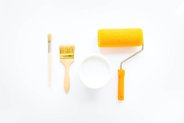 Vernice bianca e pennelli per la riparazione della casa e la pittura su sfondo bianco. Composizione minimalista bianca e gialla. Posa piatta, vista dall'alto
 - Foto, immagini