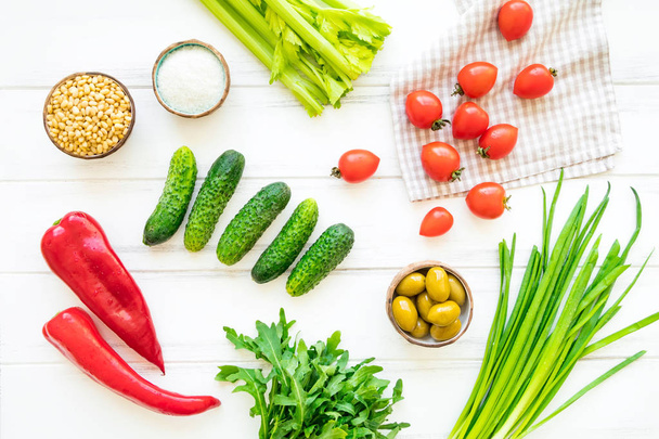 Ingredients for healthy lunch with herbs and vegetables, bright background. Tomatos, cucumbers, onions, celery, sweet pepper, rocket salad, salt, pine nuts and olives. Flat lay, view from above - Фото, изображение