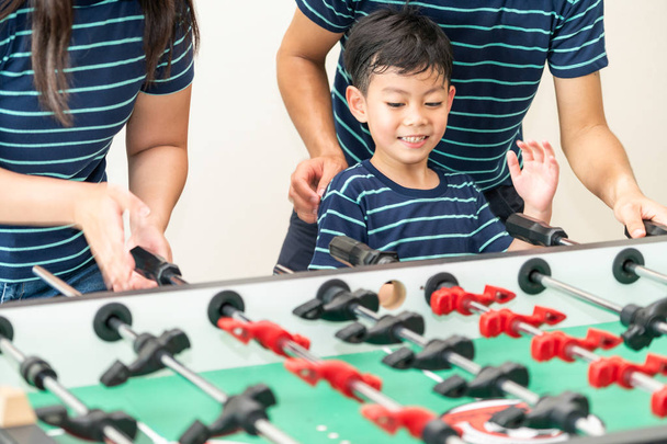 Happy kid playing foosball table soccer with family, father and mother. - 写真・画像