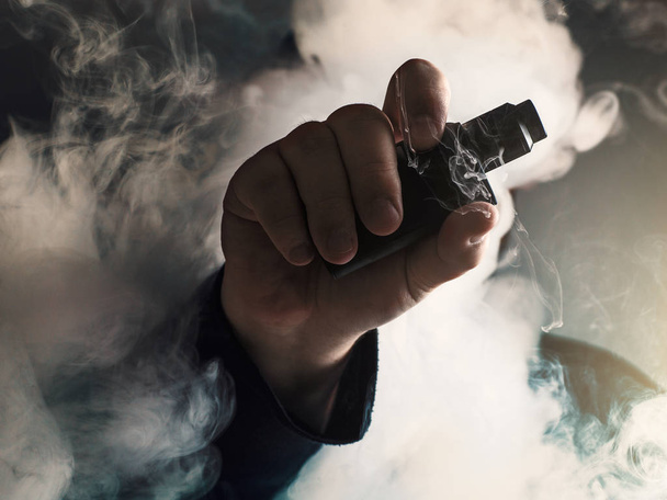 Homem mão mostra dispositivo vape na nuvem de fundo de vapor. Conceito de violação
 - Foto, Imagem