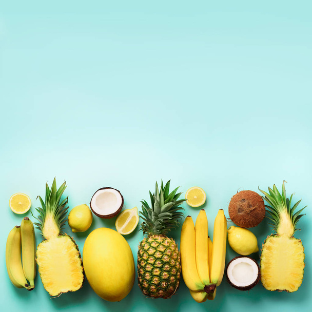 Fresh organic yellow fruits over blue background. Square crop. Monochrome concept with banana, coconut, pineapple, lemon, melon. Top view. Copy space. Pop art design, creative summer design. - Photo, image