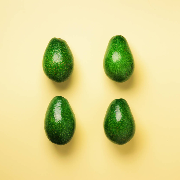 Green avocado pattern on yellow background. Top view. Square crop. Pop art design, creative summer food concept. Organic avocadoes in minimal flat lay style. - Fotoğraf, Görsel