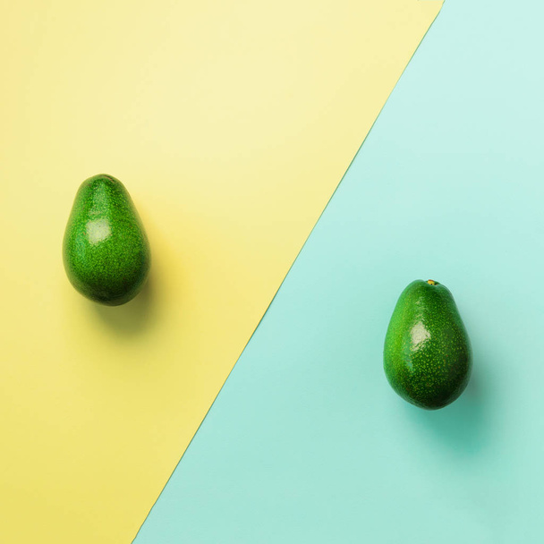 Avocado sliced with seed, whole fruit on blue and yellow background. Top view. Square crop. Pop art design, creative summer food concept. Minimal flat lay style. - Photo, image