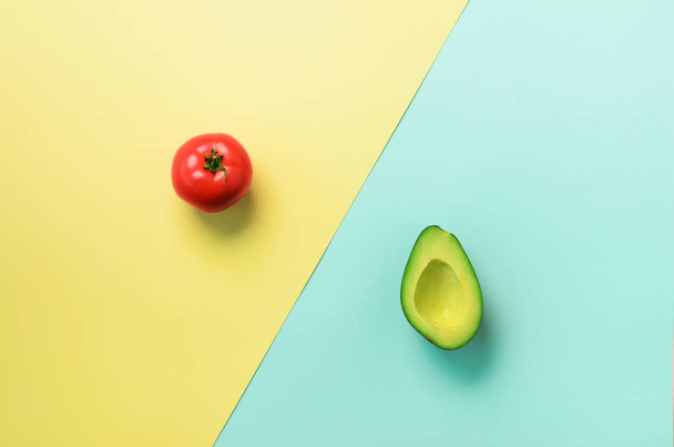 Green sliced avocado and red tomato on blue and yellow background. Top view. Pop art design, creative summer food concept. Minimal flat lay style. - Foto, imagen