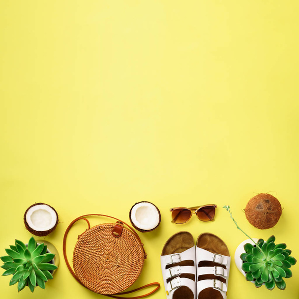 Stylish rattan bag, coconut, birkenstocks, succulent, sunglasses on yellow background. Banner. Top view with copy space. Trendy bamboo bag and white shoes. Summer fashion flat lay - Foto, imagen