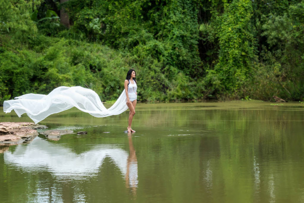 Asian woman with white dress relaxing and standing at tropical exotic river with turquoise amazing color water in beautiful destination forest. Lifestyle Concept - Fotó, kép