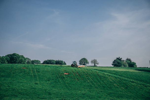 29. Mai 2018, Kork, Irland - ein Traktor pflügt an einem sonnigen Tag das Gras auf den Feldern - Foto, Bild