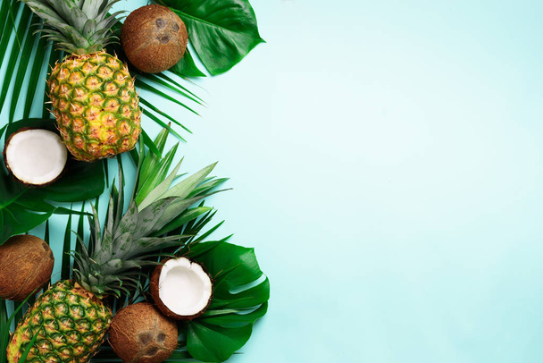 Exotic pineapples, ripe coconuts, tropical palm and green monstera leaves on blue background with copyspace for your text. Creative layout. Summer concept. Flat lay, top view - Photo, Image