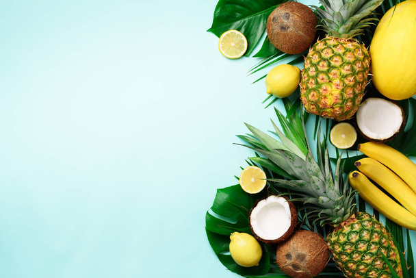 Exotic pineapples, ripe coconuts, banana, melon, lemon, tropical palm and green monstera leaves on blue background with copyspace for your text. Creative layout. Summer concept. Flat lay, top view - Photo, image