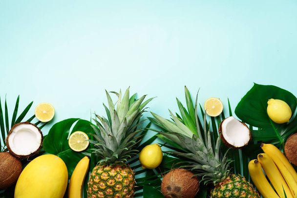 Exotic pineapples, ripe coconuts, banana, melon, lemon, tropical palm and green monstera leaves on blue background with copyspace for your text. Creative layout. Summer concept. Flat lay, top view - Fotoğraf, Görsel