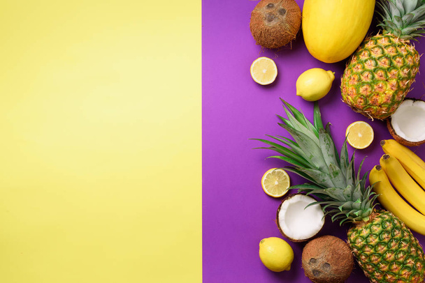 Exotic pineapples, coconuts, banana, melon, lemon, tropical palm and green monstera leaves on yellow, purple background with copyspace. Creative layout. Monochrome summer concept. Flat lay, top view - Photo, image