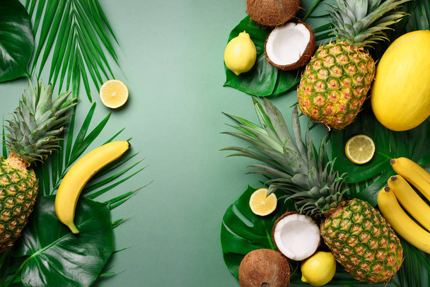 Exotic pineapples, coconuts, banana, melon, lemon, tropical palm and monstera leaves on green, turquoise background with copyspace. Creative layout. Monochrome summer concept. Flat lay, top view. - Foto, afbeelding