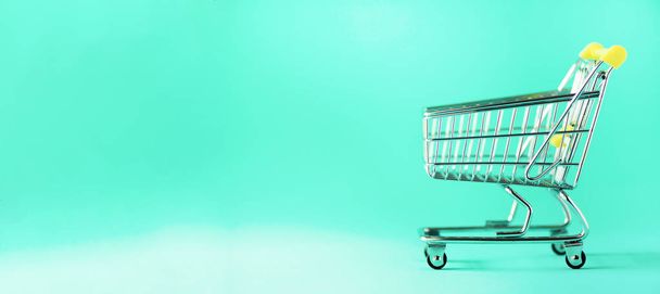 Shopping cart on blue background. Minimalism style. Creative design. Copy space. Banner. Shop trolley at supermarket. Sale, discount, shopaholism concept. Consumer society trend - Zdjęcie, obraz