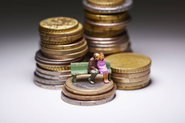 Velhice sem conceito de falta de dinheiro com a família sênior sentada em um banco acima de pilhas de moedas
 - Foto, Imagem