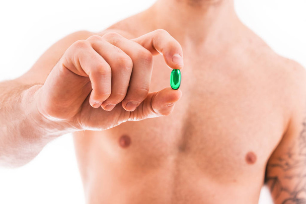 白い背景に分離された緑色の錠剤を保持している筋肉の若い男. - 写真・画像
