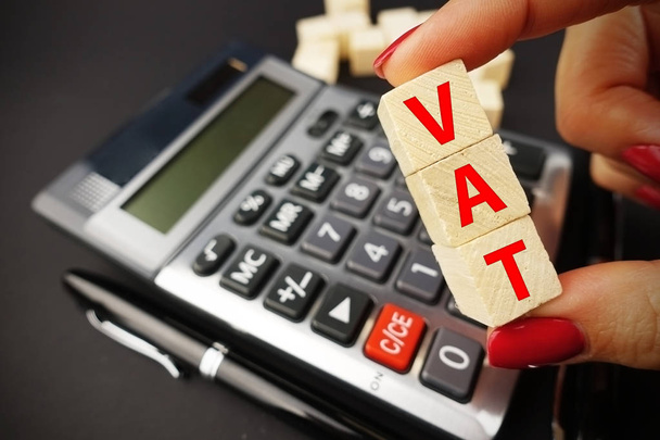Podatku VAT tekst na drewniane kostki powyżej Kalkulator biuro sugeruje czas podatku lub zapłaty - Zdjęcie, obraz