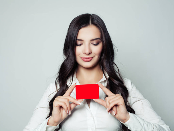 Mulher de negócios feliz com cartão vazio vermelho. Jovem mulher sorrindo e segurando cartão em branco em suas mãos, conceito de negócios e educação
 - Foto, Imagem