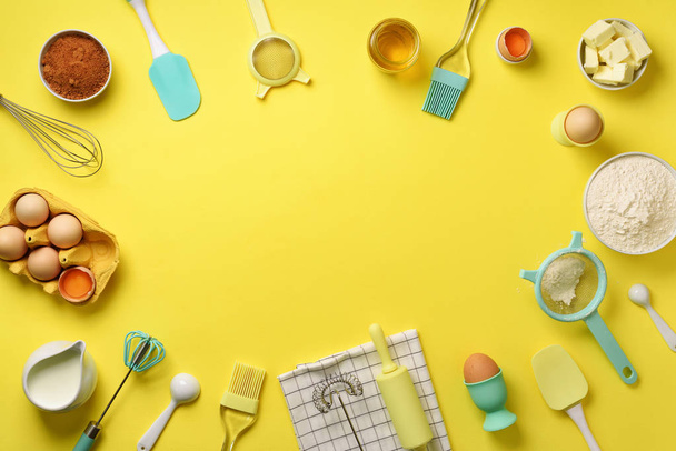 Time to bake. Baking ingredients - butter, sugar, flour, eggs, oil, spoon, rolling pin, brush, whisk, towel over yellow background. Bakery food frame, cooking concept. Top view, copy space. Flat lay - Photo, image