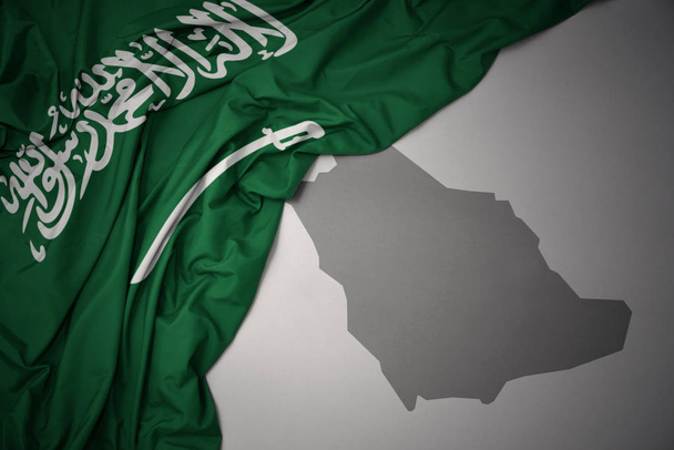 κουνώντας πολύχρωμο εθνική σημαία της Σαουδικής Αραβίας σε φόντο γκρι Χάρτης. - Φωτογραφία, εικόνα