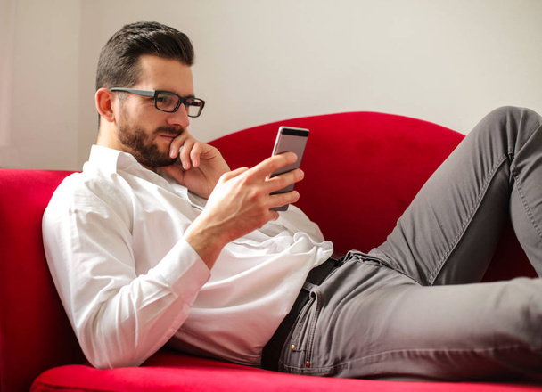 Businessman lying on a sofa with a smartphone. - Foto, afbeelding