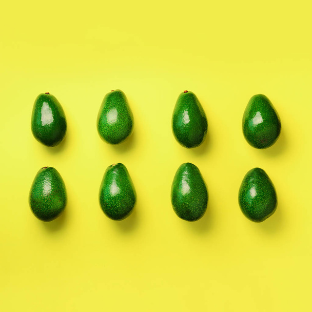 Green avocado pattern on yellow background. Square crop. Top view. Pop art design, creative summer food concept. Organic avocadoes in minimal flat lay style. - Фото, зображення