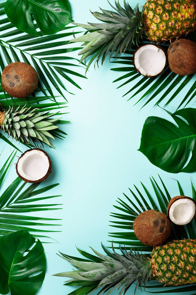 Exotic pineapples, ripe coconuts, tropical palm and green monstera leaves on blue background with copyspace for your text. Creative layout. Summer concept. Flat lay, top view - 写真・画像