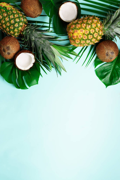 Exotic pineapples, ripe coconuts, tropical palm and green monstera leaves on blue background with copyspace for your text. Creative layout. Summer concept. Flat lay, top view - Φωτογραφία, εικόνα