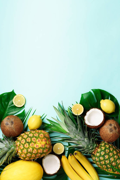 Exotische ananas, rijpe kokosnoten, banaan, meloen, citroen, tropische palm en groene monstera laat op blauwe achtergrond met copyspace voor uw tekst. Creatieve lay-out. Zomer concept. Plat lag, top uitzicht - Foto, afbeelding