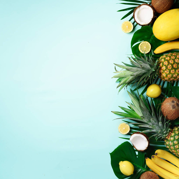 Exotic pineapples, ripe coconuts, banana, melon, lemon, tropical palm and monstera leaves on blue background with copyspace for text. Square crop. Creative layout. Summer concept. Flat lay, top view - 写真・画像