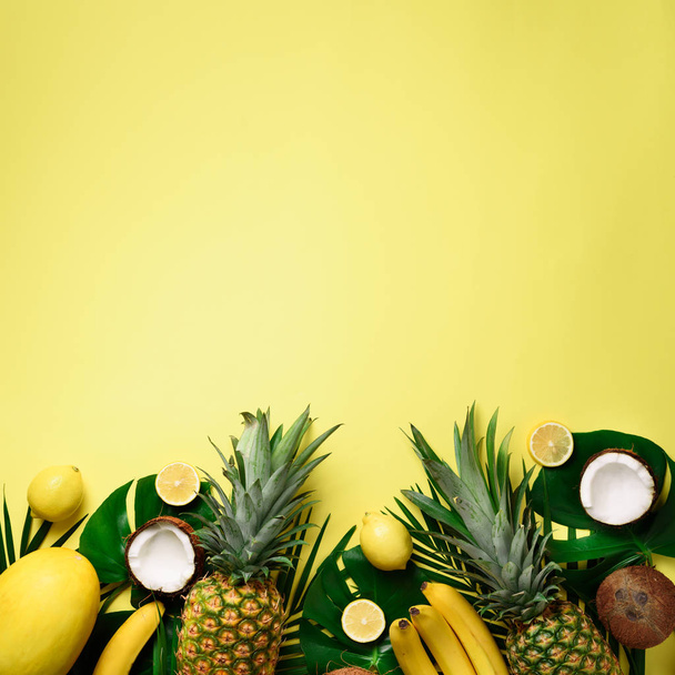 Exotic pineapples, ripe coconuts, banana, melon, lemon, tropical palm and green monstera leaves on yellow background with copyspace. Creative layout. Monochrome summer concept. Flat lay, top view. - Fotografie, Obrázek