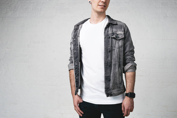 Handsome young guy wearing blank t-shirt and jacket, white bricks wall background - Foto, imagen