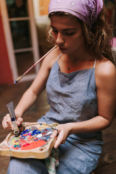 Binnen schot van professionele vrouwelijke artiest schilderij op doek in de studio met een borstel in haar mond. - Foto, afbeelding