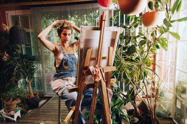Indoor shot of professional female artist painting on canvas in studio with plants. - Foto, afbeelding