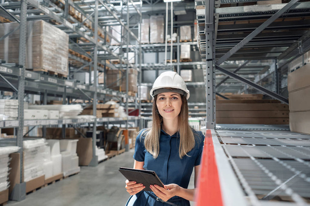 Beautiful young woman worker of furniture store in shopping center. Girl looking for goods with a tablet is checking inventory levels in a warehouse. Logistics concept - Photo, Image
